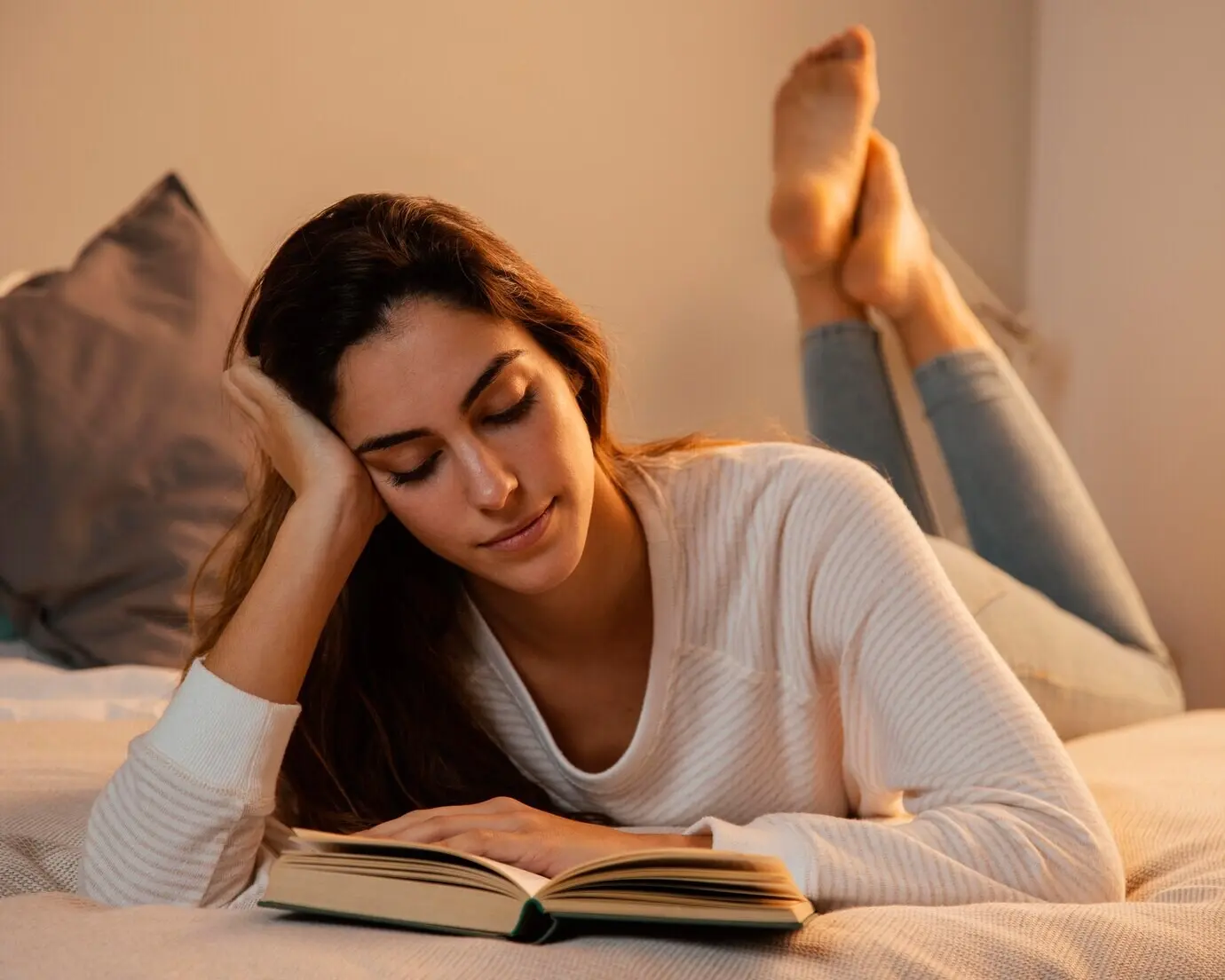 Front-facing view of a woman reading a book in bed at home.