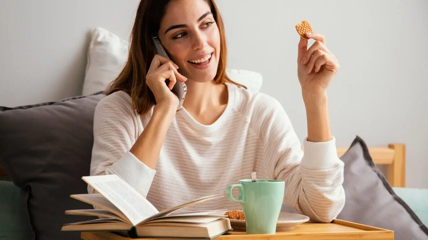 A woman has breakfast at home while talking on the phone.
